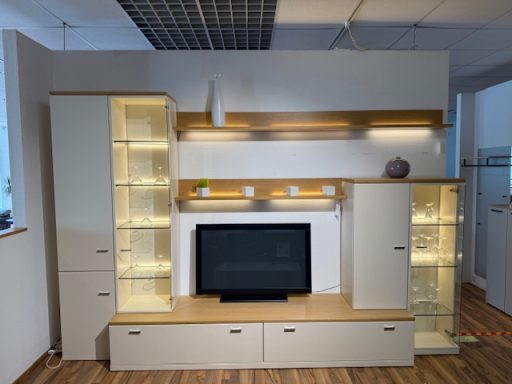 Moderne Wohnwand mit TV, Regalen und beleuchteten Glaskästen in neutralen Farben.